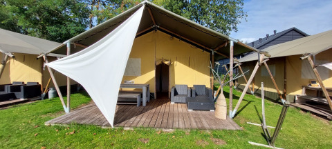 Lodge de tienda safari con terraza de madera, muebles de exterior y lona, rodeado de césped y árboles.