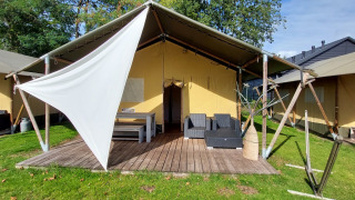 Safaritent lodge met houten terras, tuinmeubilair en schaduwdoek, gelegen op een groene grasmat.