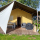 Safari telt lodge med træterrasse, havemøbler og skyggeelement, omgivet af grønne græsplæner og træer.