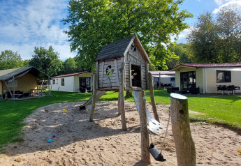 Legeplads med træhus på sand, omgivet af safari-telt og hytter ved Vakantiepark De Luttenberg, Holland.