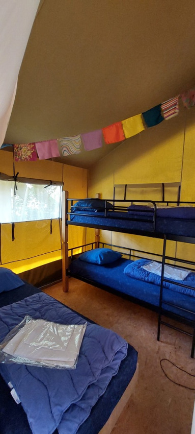 Interior de tienda safari en Vakantiepark De Luttenberg con literas, cama doble y banderines de colores.