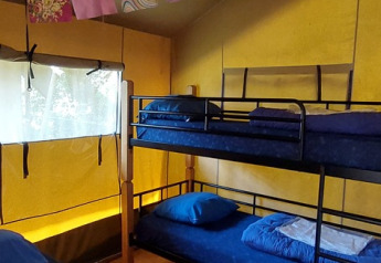 Indvendig af en safaritelthytte på Vakantiepark De Luttenberg med køjeseng, dobbeltseng og farverige flag.