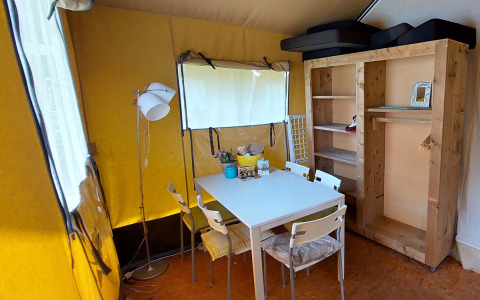 Interior de una tienda safari con mesa comedor, sillas, armario de madera y paredes de lona amarilla.