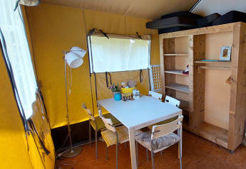 Indendørsbillede af en Safari-teltlodge med spisebord, stole, trægarderobe og gul teltvæg.
