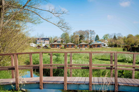 Wooden bridge over grassy field leading to safari tents at Camping Waddenzee holiday park in North Holland, NL.