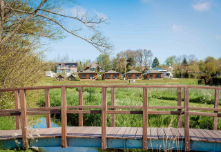 Holzbrücke über grünes Feld mit Safari-Zelten im Camping Waddenzee, Nordholland, Niederlande, im Hintergrund.