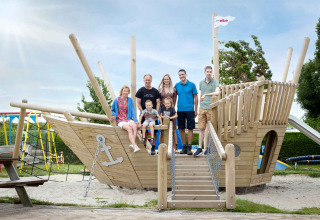 Familie auf einem großen Holzspielplatzschiff bei Camping Waddenzee in Nordholland, Niederlande, posierend.