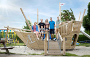 Famiglia che posa su una grande nave parco giochi in legno al Camping Waddenzee, Olanda Settentrionale, Paesi Bassi.