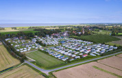 Luftfoto af Camping Waddenzee feriepark med campingvogne og grønne marker i Nordholland, Holland.
