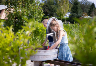 Zwei Kinder spielen an einem Outdoor-Wasserspiel im Ferienpark Camping Waddenzee in Nordholland.