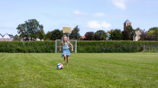 Niña jugando al fútbol en el campo de Camping Waddenzee en Holanda Septentrional, iglesia al fondo.
