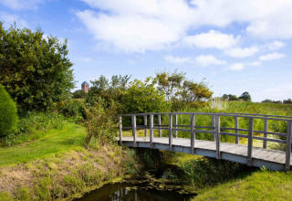 Pont en bois au-dessus d’un ruisseau au Camping Waddenzee, paysage verdoyant et ciel bleu en Hollande du Nord.