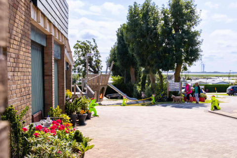 Escena en Camping Waddenzee, North Holland, Países Bajos con parque infantil, flores y visitantes al aire libre.