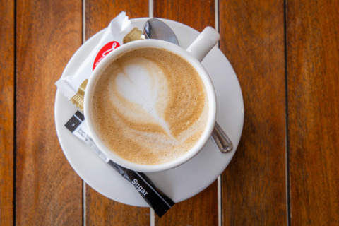 En kop cappuccino med latte art, sukkerpakker og en kiks på en træbord ved Camping Waddenzee, Holland.