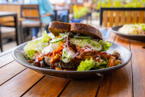 Delicious sandwich with lettuce, meat, bread, and fresh veggies on a black plate at Camping Waddenzee.