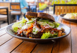 Delicious sandwich with lettuce, meat, bread, and fresh veggies on a black plate at Camping Waddenzee.