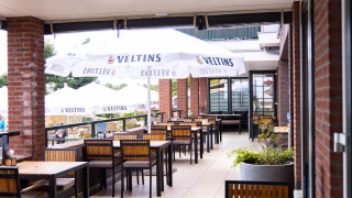 Zona de comedor exterior con mesas, sillas y sombrillas en Camping Waddenzee, parque en Holanda del Norte.