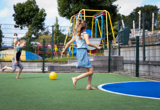 Kinder spielen barfuß Fußball auf einem Spielplatz im Ferienpark Camping Waddenzee in Nordholland, Niederlande.