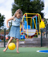 Mädchen spielt barfuß mit einem gelben Ball auf dem Spielplatz im Camping Waddenzee, Holland.