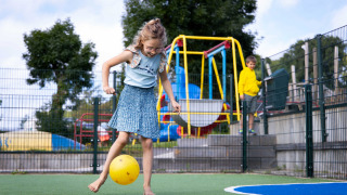 Niña jugando descalza con una pelota amarilla en el parque infantil de Camping Waddenzee, Países Bajos.