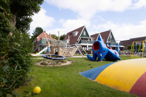 Niños jugando en un parque infantil con tobogán, trampolín y estructuras coloridas en Camping Waddenzee.