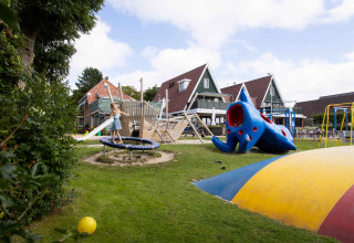 Børn leger på legeplads med rutchebane, trampolin og farverige strukturer ved feriepark Camping Waddenzee.