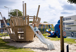 Speeltuin bij Camping Waddenzee met piratenboot, glijbaan en spelende kinderen in Noord-Holland, Nederland.