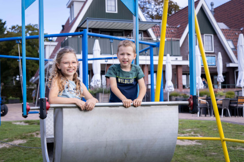Dos niños sonríen y juegan en el parque infantil de Camping Waddenzee, parque vacacional en Holanda Septentrional.