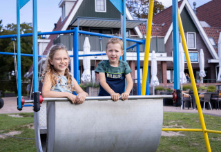Two children smile and play on a playground at Camping Waddenzee holiday park in North Holland, Netherlands.