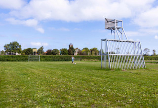 Et grønt fodboldfelt på Camping Waddenzee i Holland med mærkelige mål og basketballkurve.