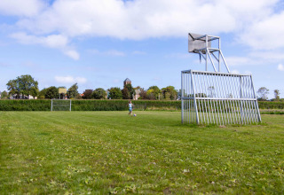 A grassy sports field at Camping Waddenzee, Netherlands, showing odd goals and basketball hoops.