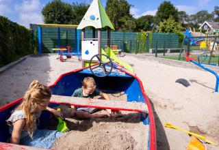 Twee kinderen spelen in een bootvormige zandbak bij Camping Waddenzee in Noord-Holland, Nederland.