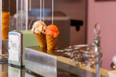 Two ice cream cones with one scoop each—cookie and strawberry—on a counter in an ice cream shop.