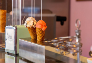 Two ice cream cones with one scoop each—cookie and strawberry—on a counter in an ice cream shop.