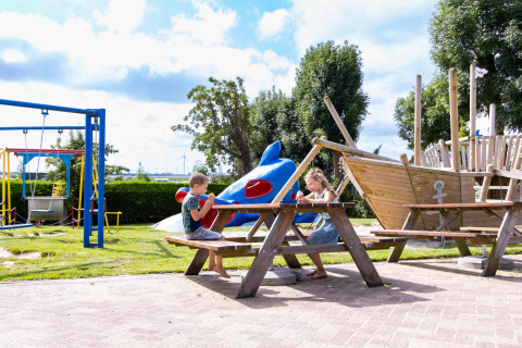 Two children enjoy ice cream at a picnic table on a playground at Camping Waddenzee, North Holland.