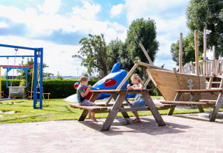 To børn spiser is ved et picnicbord i en legeplads med skib og gynge på Camping Waddenzee, Holland.