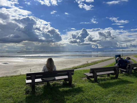 Eine Person sitzt auf einer Bank und blickt auf das Wasser bei Scherpenisse, Zeeland, Niederlande, unter dramatischen Wolken.