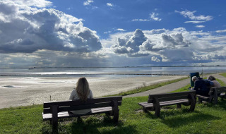 Una persona se sienta en un banco mirando el agua cerca de Scherpenisse, Zelanda, Países Bajos, bajo nubes dramáticas.