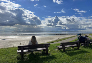 Une personne est assise sur un banc devant l'eau près de Scherpenisse, Zélande, Pays-Bas, sous un ciel nuageux.