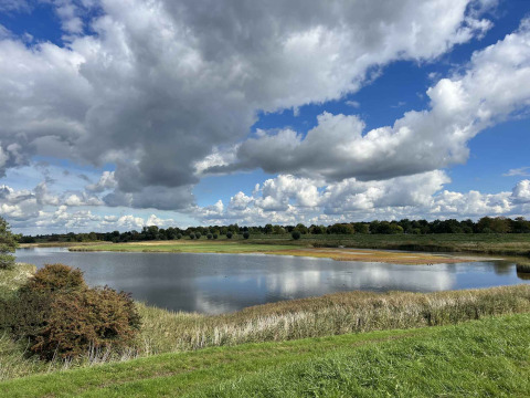 Vista de un lago tranquilo, hierba verde y nubes dramáticas en Vakantiepark de Zeeuwse Parel, Zeeland.