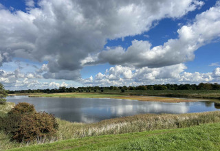 Vista de un lago tranquilo, hierba verde y nubes dramáticas en Vakantiepark de Zeeuwse Parel, Zeeland.