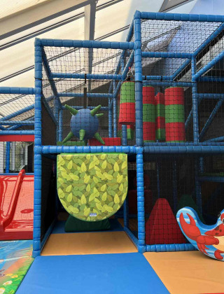 Zona de juegos interior en Vakantiepark de Zeeuwse Parel con tobogán rojo, gimnasio y decoración de cangrejo.