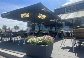 Terrazza esterna al Vakantiepark de Zeeuwse Parel in Zelanda, Paesi Bassi, con tavoli, sedie e grandi ombrelloni.