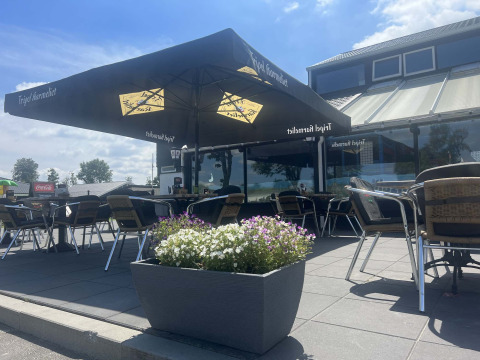 Terrasse extérieure au Vakantiepark de Zeeuwse Parel en Zélande, Pays-Bas, avec tables, chaises et grands parasols.