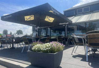 Außenterrasse im Vakantiepark de Zeeuwse Parel in Zeeland, Niederlande, mit Stühlen, Tischen und Sonnenschirmen.