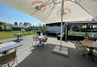 Sonnige Terrasse mit Tischen und Stühlen im Vakantiepark de Zeeuwse Parel, Zeeland, Niederlande.