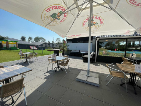 Terraza soleada con mesas, sillas y sombrilla en Vakantiepark de Zeeuwse Parel en Zeeland, Países Bajos.