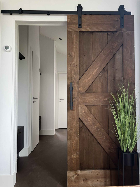 Entrada a una cabaña en De Parel, Vakantiepark de Zeeuwse Parel, con puerta corrediza rústica y planta decorativa.
