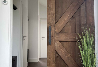 Entrée d’un lodge à De Parel, Vakantiepark de Zeeuwse Parel, avec porte coulissante en bois rustique et plante.