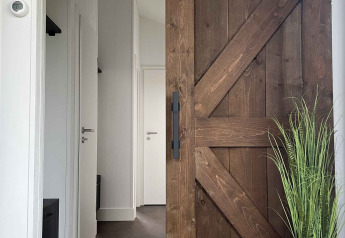 Entrada a una cabaña en De Parel, Vakantiepark de Zeeuwse Parel, con puerta corrediza rústica y planta decorativa.